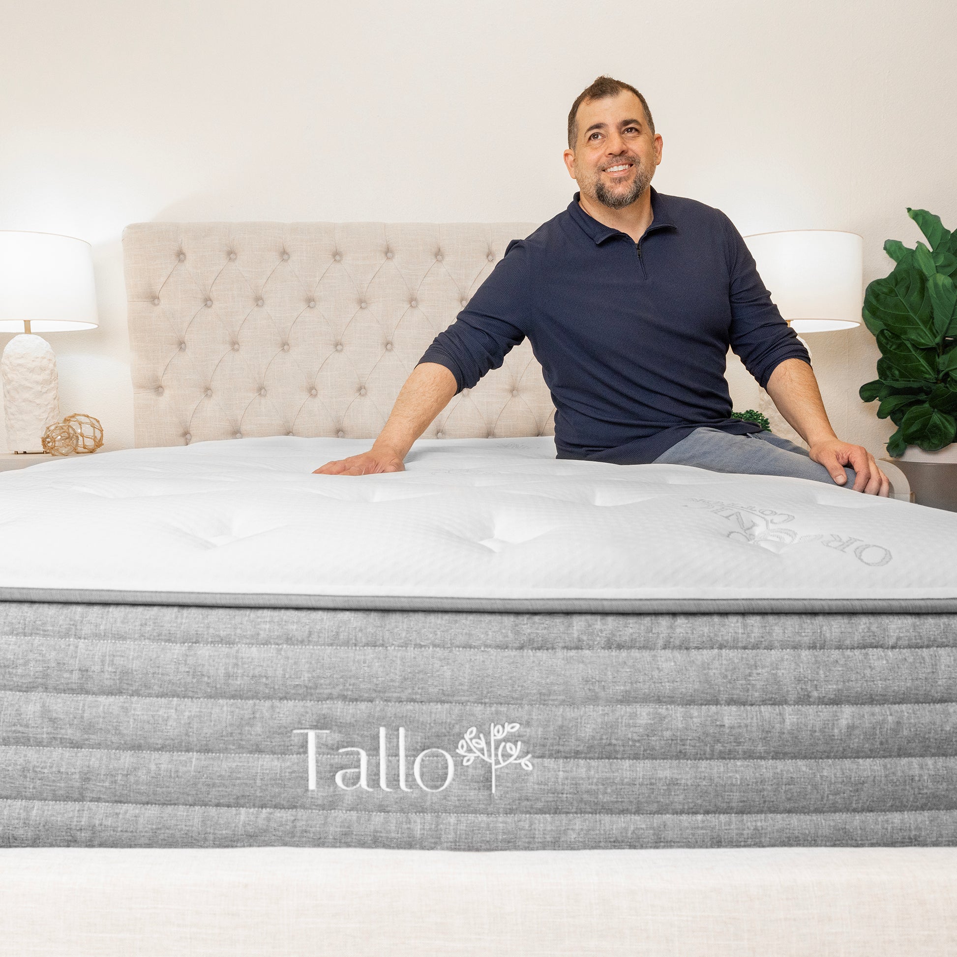 Man sitting on Tallo Classic Mattress, smiling, relaxed, comfortable sleep, organic mattress, eco-friendly materials, supportive mattress, happy customer
